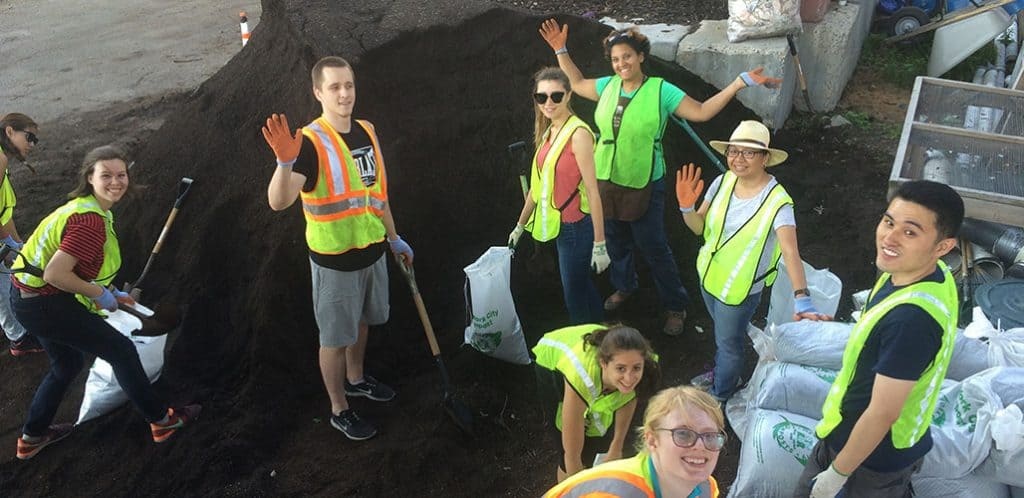 Volunteers wave in front of pile of finished compost
