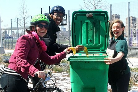 Three people smile widely as they deposit scraps into a bin.