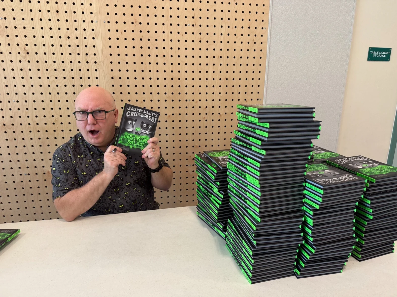 An author beside stacks of new books for students