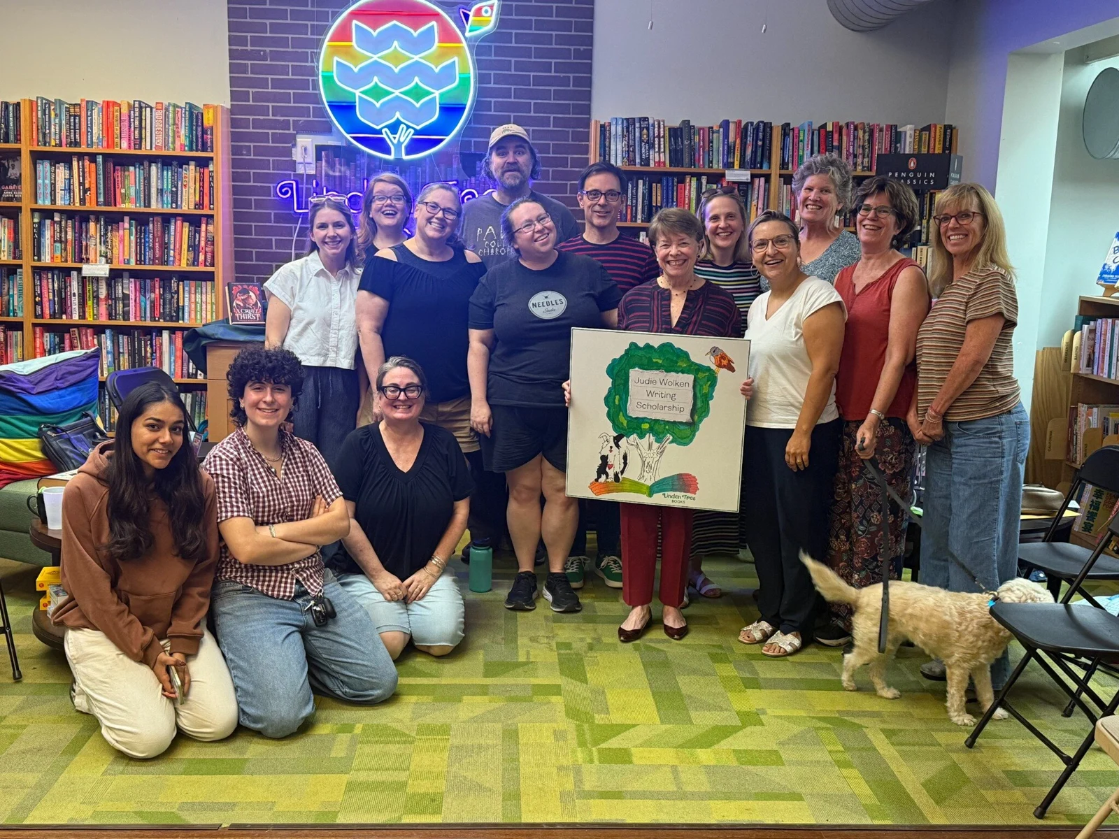 Judie Wolken surrounded by the Linden Tree Books team while holding artwork for the Judie Wolken Writing Scholarship