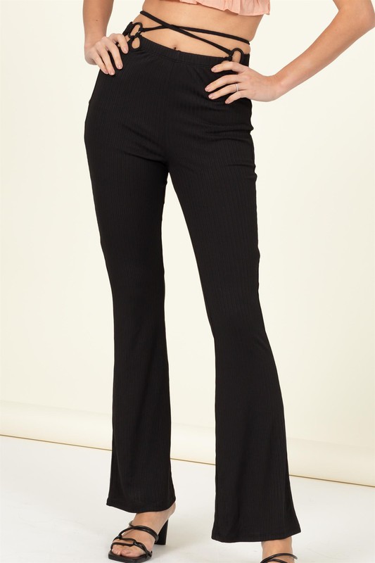 See a pair of ribbed black semi-flared pants with key ring cutouts on either side of the waist. 