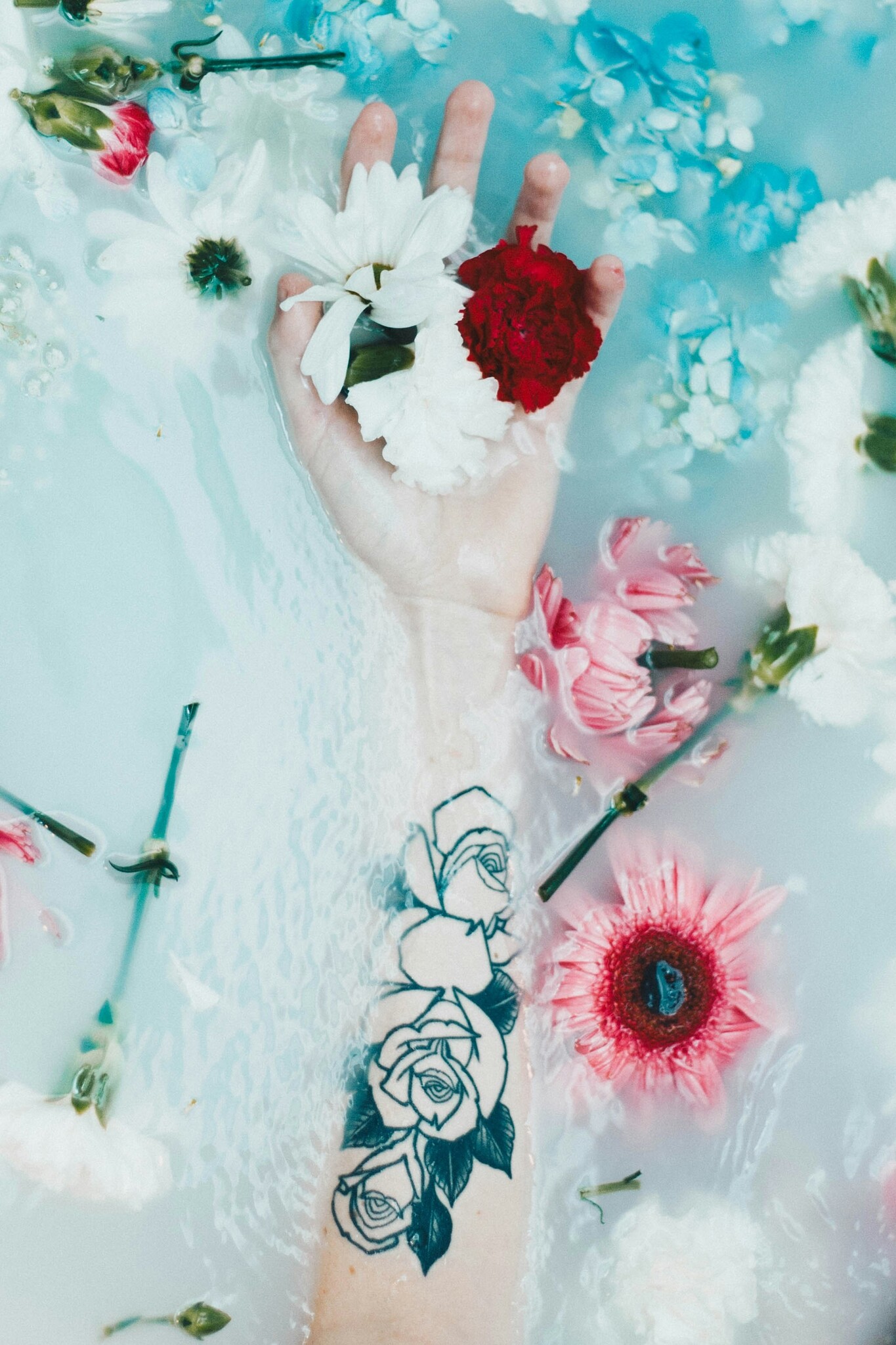 Arm holding flowers in a bath. Photo by Grace Madeline on Unsplash