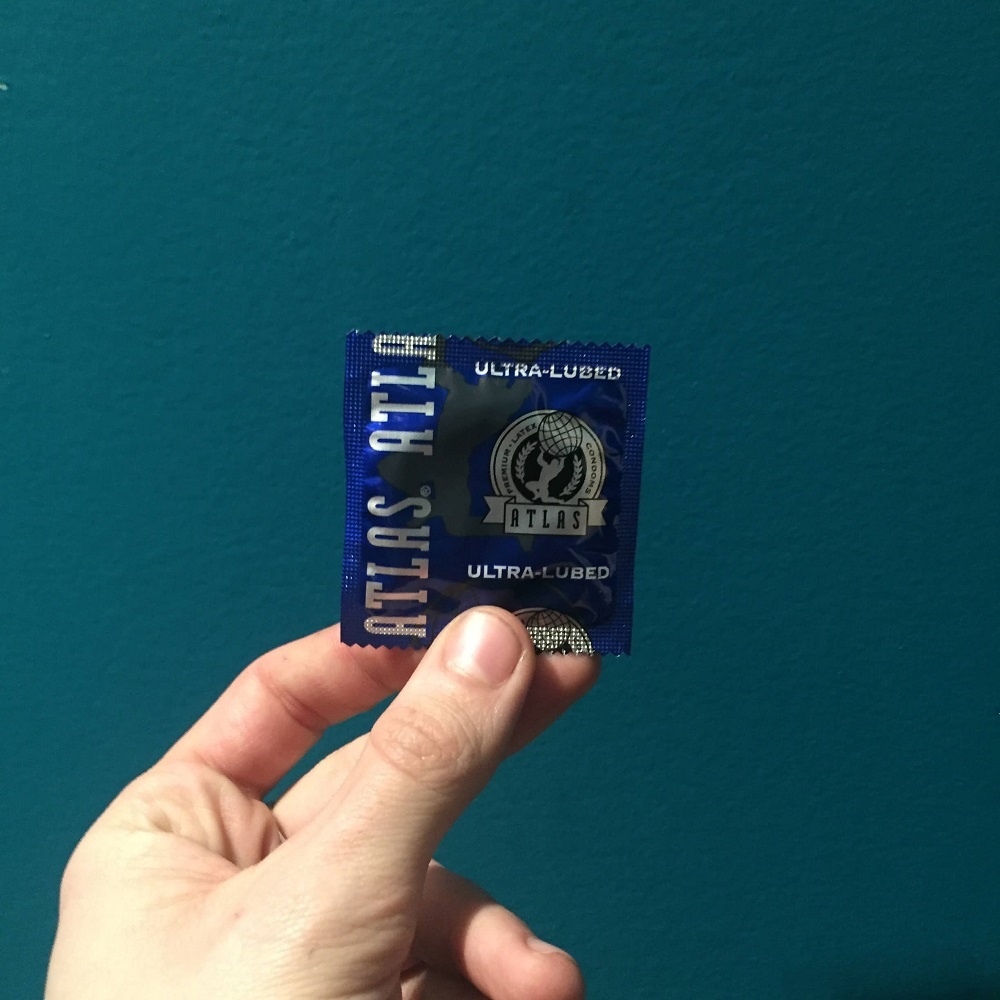 A hand holds a packaged Atlas Ultra Lubed Condom