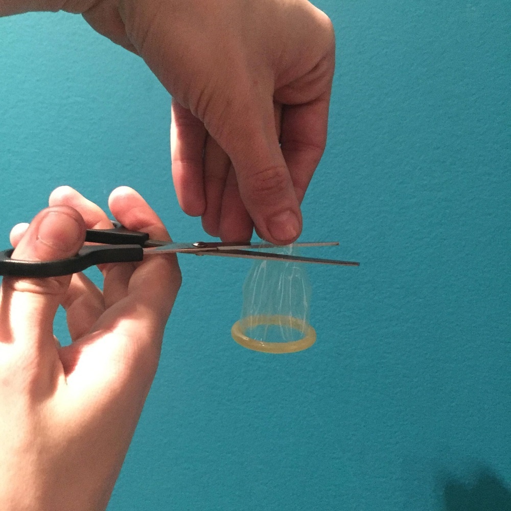 The now unpackaged condom has been unrolled about an inch, and the model holds an open pair of scissors about to cut off the reservoir.