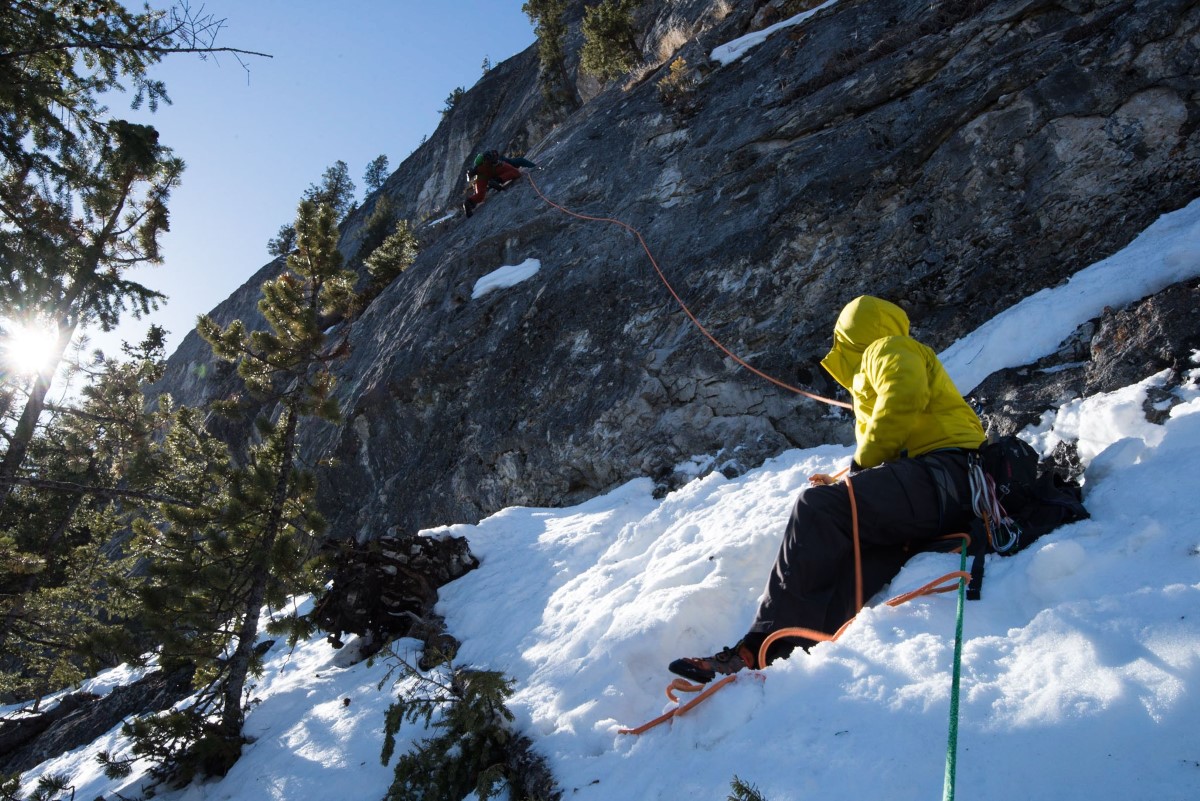 Man sitting in the snow, belaying a rock climber