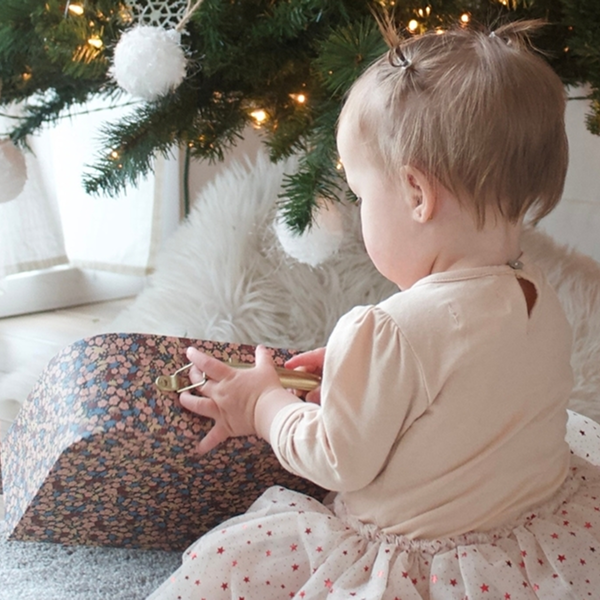 Une petite fille assise sur le sol près d'un sapin de Noël, vêtue d'un habit d'hiver.