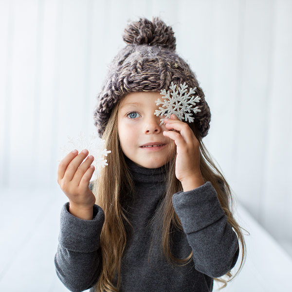 Une jeune fille portant un bonnet en tricot tient un flocon de neige, illustrant les tenues de réveillon enfants 2025.