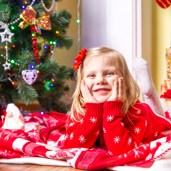 Une petite fille en pull rouge allongée sur le sol, portant des pyjamas de Noël assortis 2025.