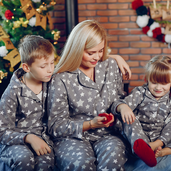 Une femme et deux enfants en pyjamas de Noël assortis, assis sur un canapé, souriant et se détendant ensemble.