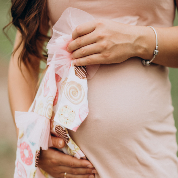 Femme enceinte tenant un vêtement pour bébé devant son ventre illustrant les indispensables de maternité