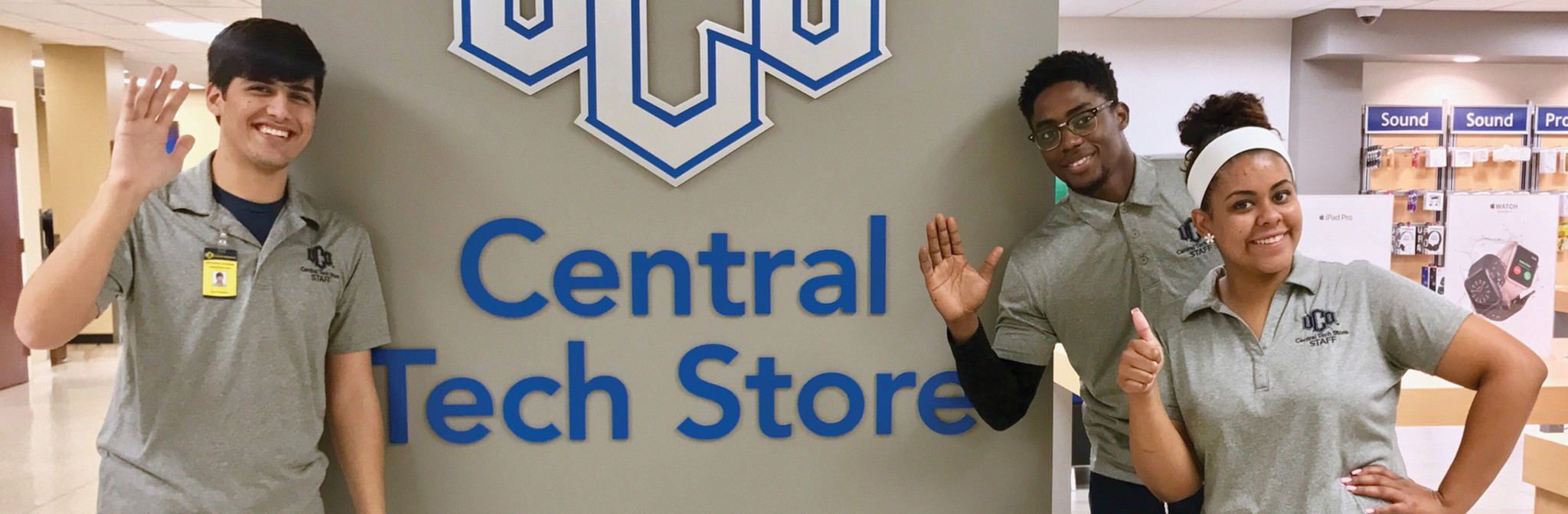 Smiling staff members in front of UCO Central Tech Store sign