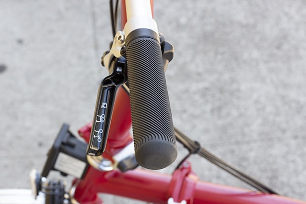 A black rubber handlebar grip with diagonal ridges in it on a red Brompton