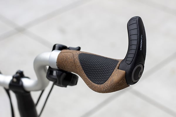 A winged cork and black rubber grip with a black plastic extension on a silver Brompton handlebar