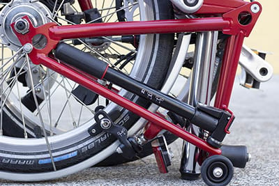 A black hand pump stored in the rear triangle of a folded red Brompton