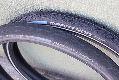 A worn tire and a brand new tire leaning against a light green wall