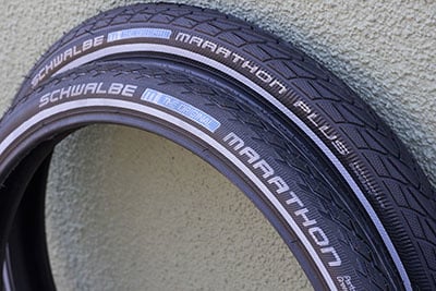 Two black tires leaning against a wall, one with the Schwalbe Marathon logo and one with the Schwalbe Marathon Plus logo