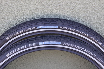Two black tires leaning against a wall, one with the Schwalbe Marathon logo and one with the Schwalbe Marathon Plus logo