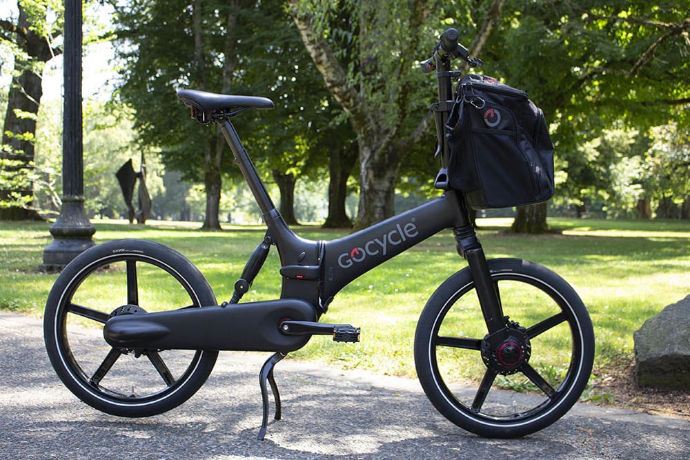 A slick-looking black folding bike with a bag on the front and a park scene in the background