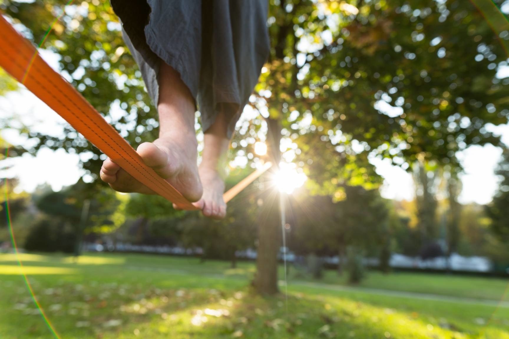 person walking across a slackline attached to two trees during the spring