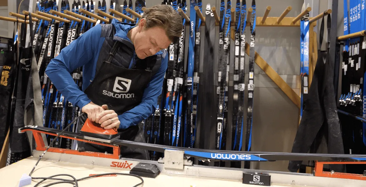 Travailleur de la marque Salomon effectuant le fartage d'un ski de fond dans un atelier.