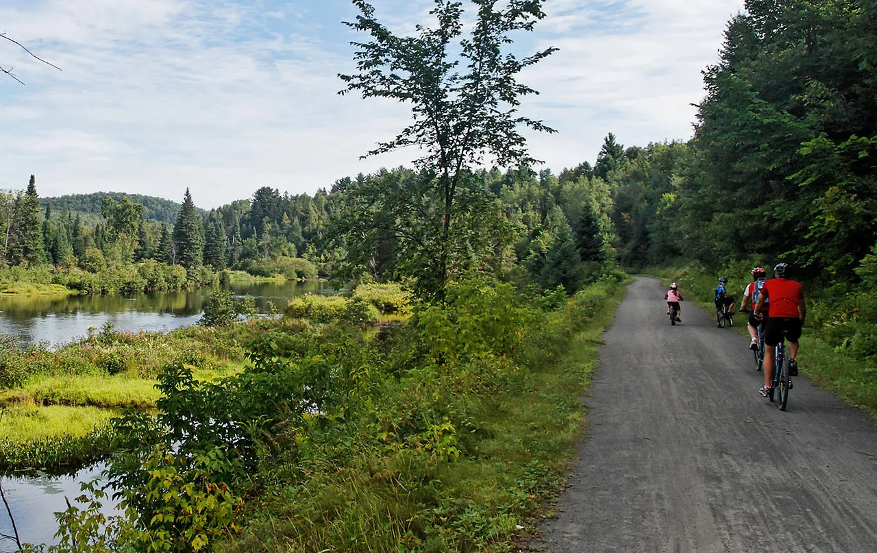 Piste cyclable du P’tit Train du Nord dans les Laurentides, entourée de végétation et montagnes.