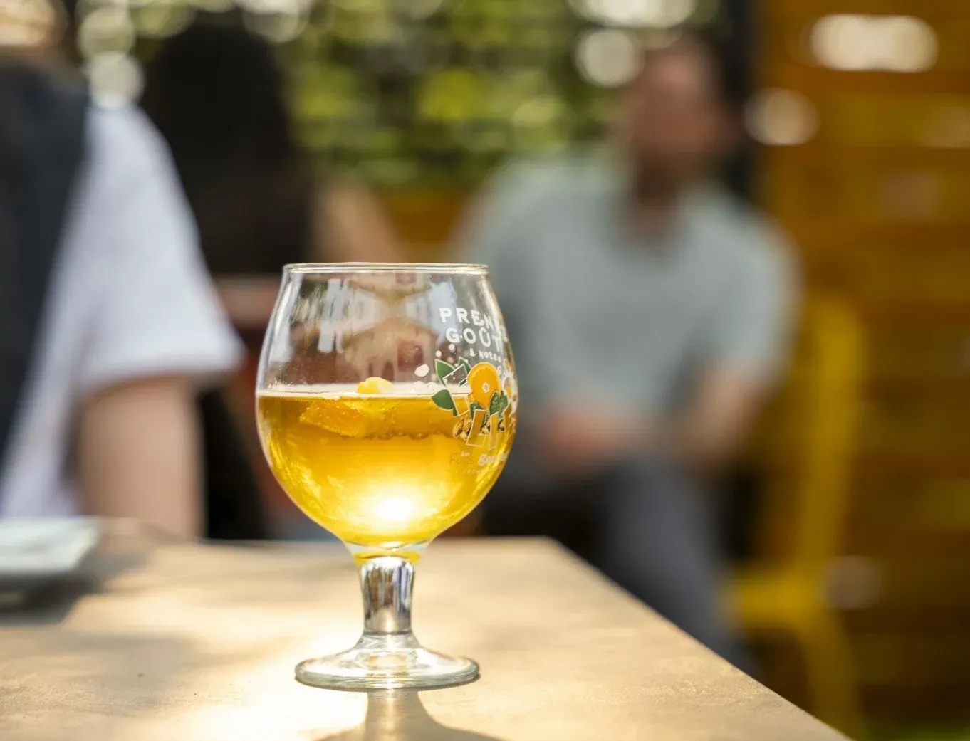 Terrasse animée de la microbrasserie Aux Fous Brassant à Rivière-du-Loup, avec verre de bière en premier plan et ambiance estivale floutée en arrière-plan.