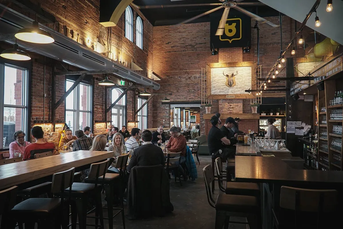 Serveur apportant une planche de dégustation de bières à un client souriant à l’intérieur du Siboire Dépôt à Sherbrooke.