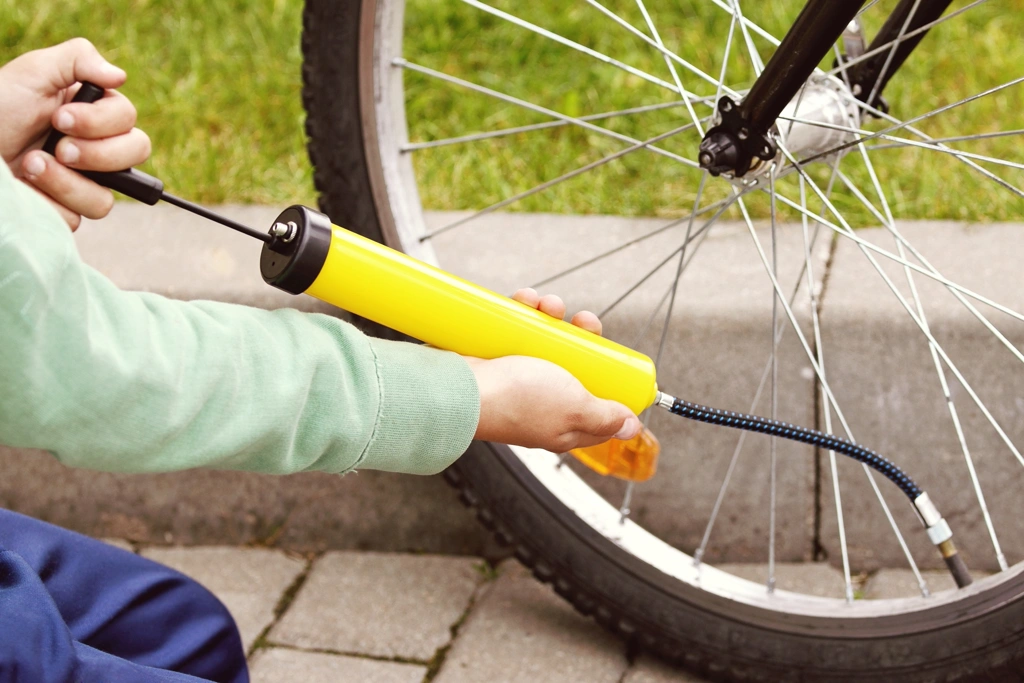 Jeune cycliste utilisant une pompe de voyage manuelle pour gonfler le pneu de son vélo sur une piste cyclable.