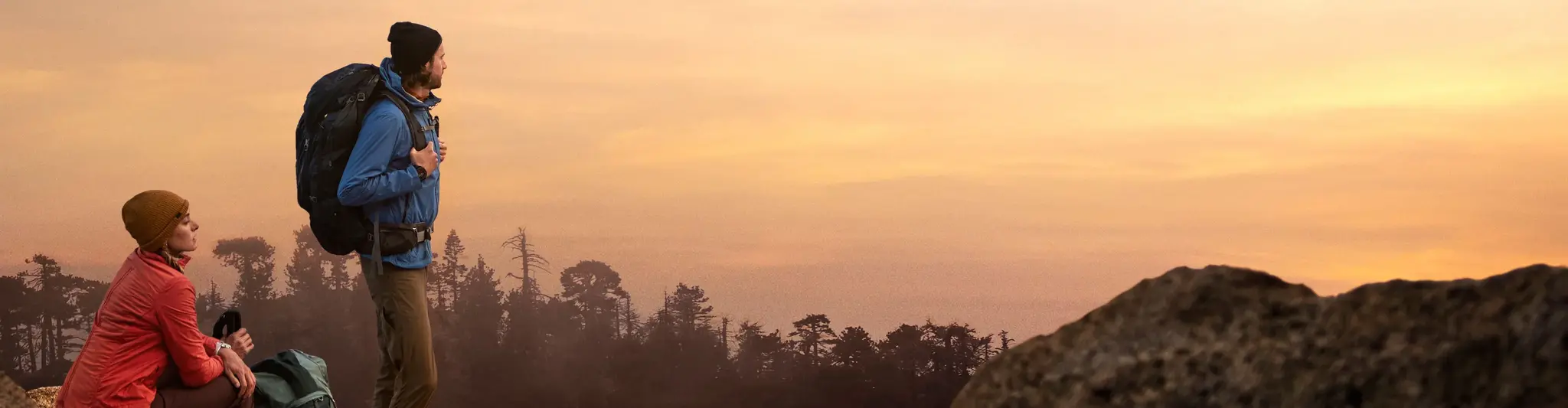 Deux randonneurs en vêtements techniques admirent le coucher de soleil, symbolisant la liberté et la préparation nécessaire pour les aventures en plein air.