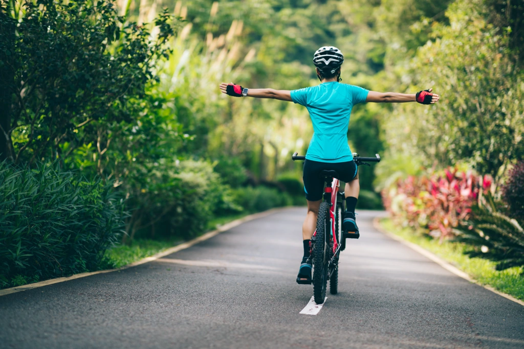 Cycliste en maillot bleu roulant sans les mains sur une piste bordée de verdure, illustrant la sensation de liberté et la réduction du stress grâce au vélo.
