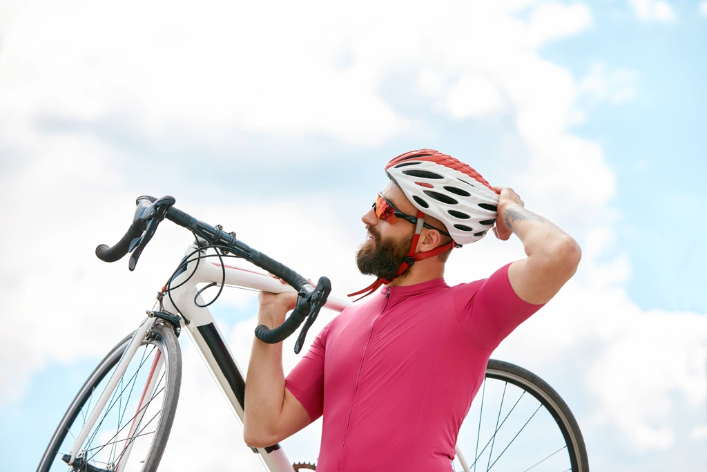 Cycliste barbu en maillot rose portant son vélo de route sur l’épaule, illustrant l’amélioration de l’endurance et de la capacité respiratoire grâce à la pratique régulière du cyclisme.