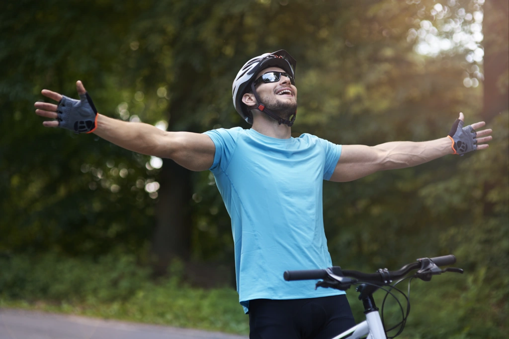 Cycliste en maillot bleu levant les bras en signe de vitalité, illustrant le renforcement du système immunitaire grâce à la pratique régulière du vélo.