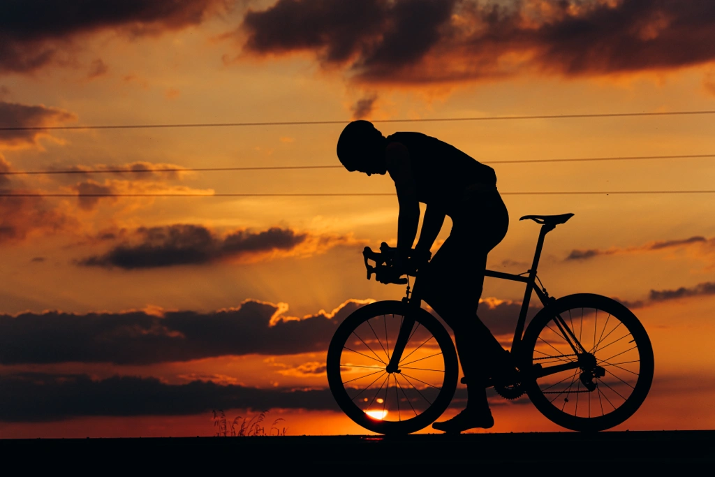 Silhouette d’un cycliste sur route au coucher du soleil, illustrant les bienfaits du vélo pour favoriser un sommeil réparateur.