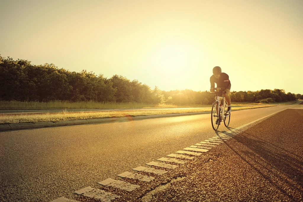Cycliste sur route au lever du soleil, illustrant la prévention des maladies chroniques comme le diabète et l’hypertension grâce au cyclisme régulier.