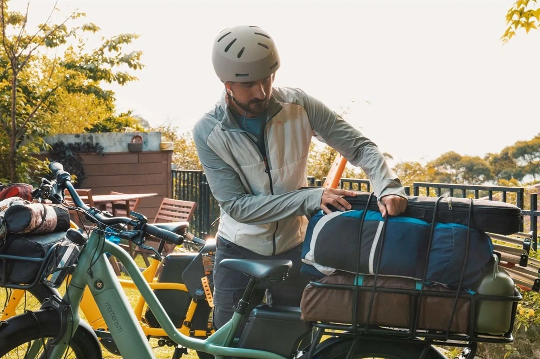 Homme ajustant un sac de voyage sur un vélo électrique cargo vert pastel, prêt pour une sortie en plein air.