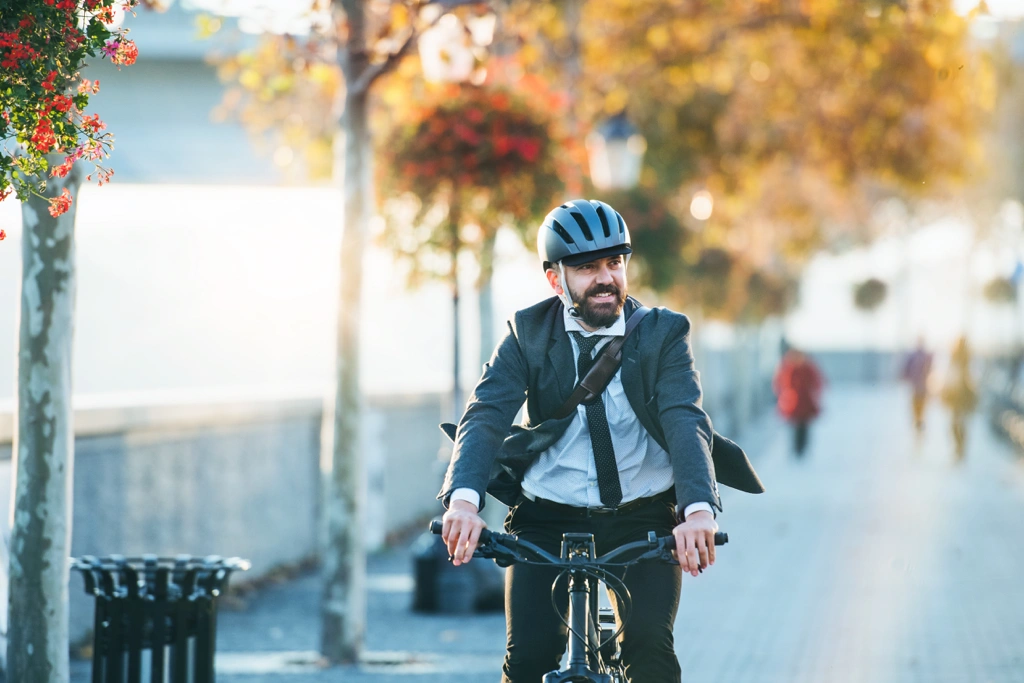 Homme en complet-cravate faisant du vélo dans une piste cyclable urbaine à l’automne au Québec, illustrant le commuting actif en 2025.