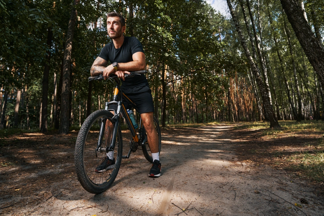 Cycliste arrêté avec son vélo sur un sentier forestier pour illustrer les causes fréquentes d’un vélo qui saute sur les chemins.