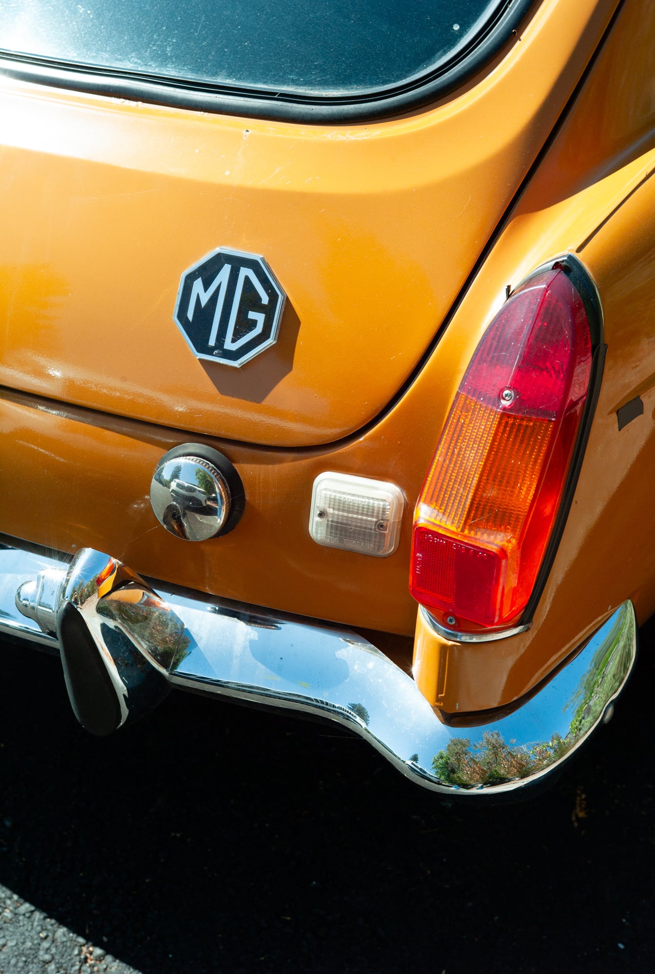 Close-up photograph of a vintage orange MG sports car showing headlight and chrome bumper