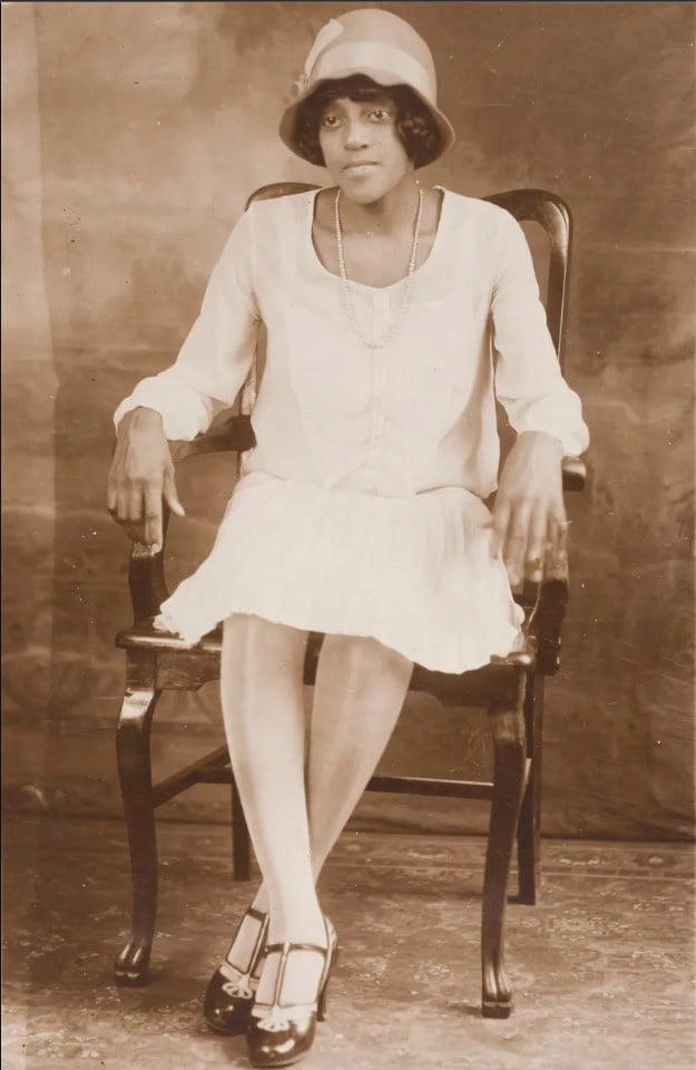 Black woman wearing a white dress and a cloche hat in the 1910s