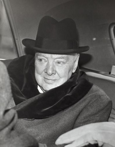 Sir Winston Churchill dans une automobile portant un manteau de fourrure et un chapeau homburg