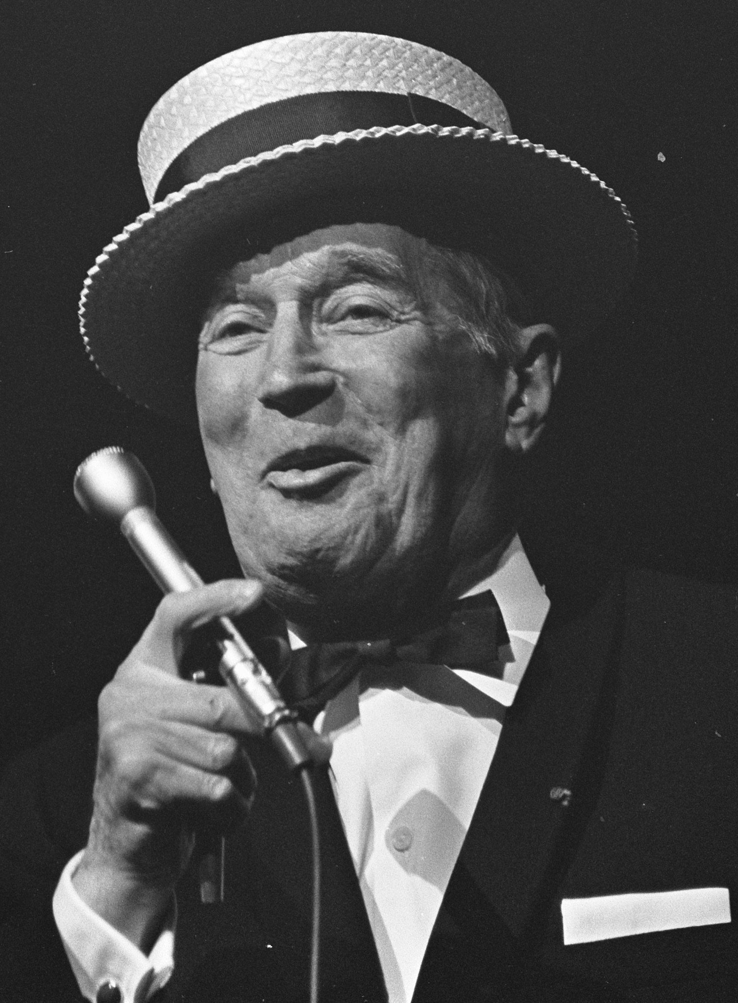 Photo noir et blanc du chanteur d'opérette Maurice Chevalier tenant un micro et portant un chapeau canotier avec un costume noir