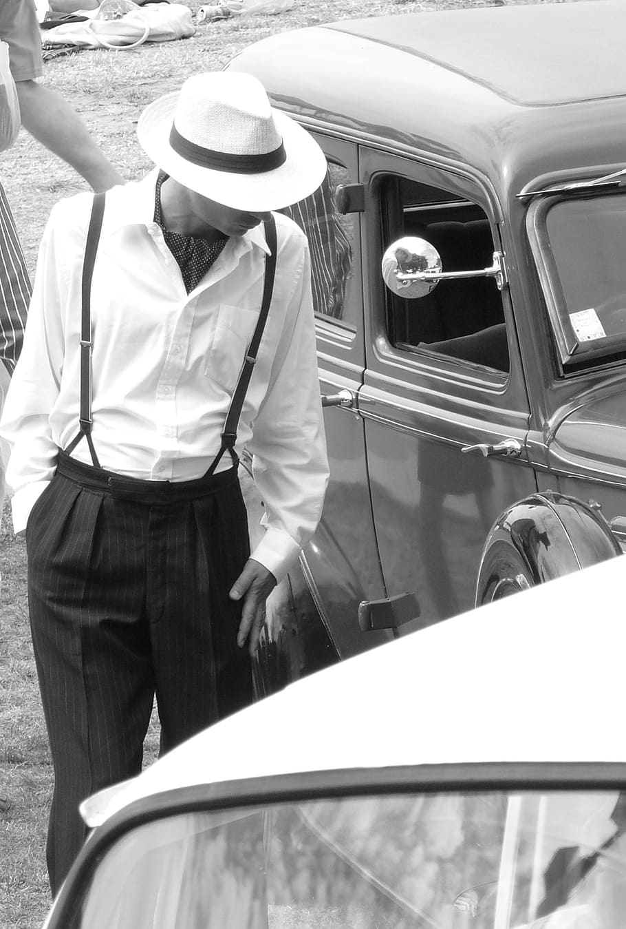 Photo noir et blanc d'un homme portant un chapeau panama blanc à côté d'une voiture ancienne