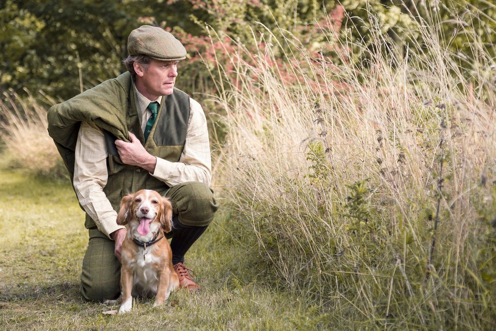 Hunter in the countryside wearing a tweed flat cap and posing with a dog