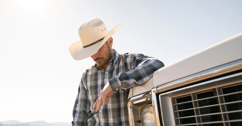 Homme avec un chapeau de cowboy large et une chemise à carreaux.