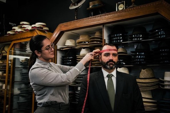 Femme mesurant le tour de tête d'un homme dans la boutique Henri Henri de Montréal