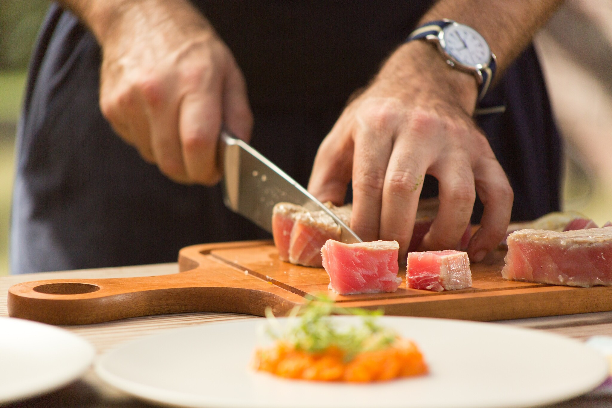 Seared tuna steak is diced into cubes on a wooden cutting board. 