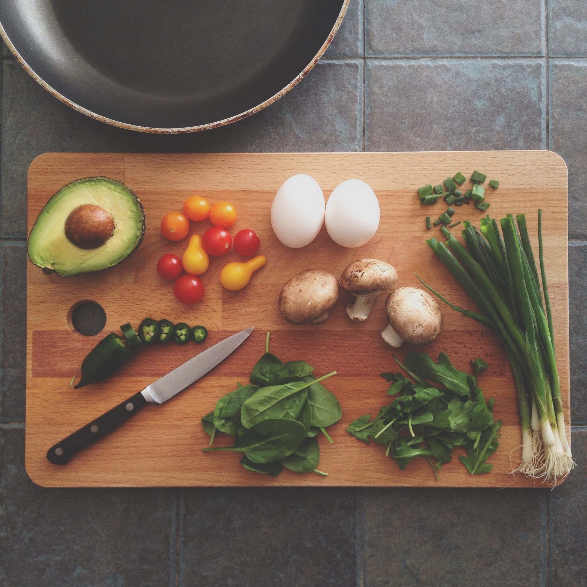 A variety of vegetables and a paring knife lie on a wood cutting board. 