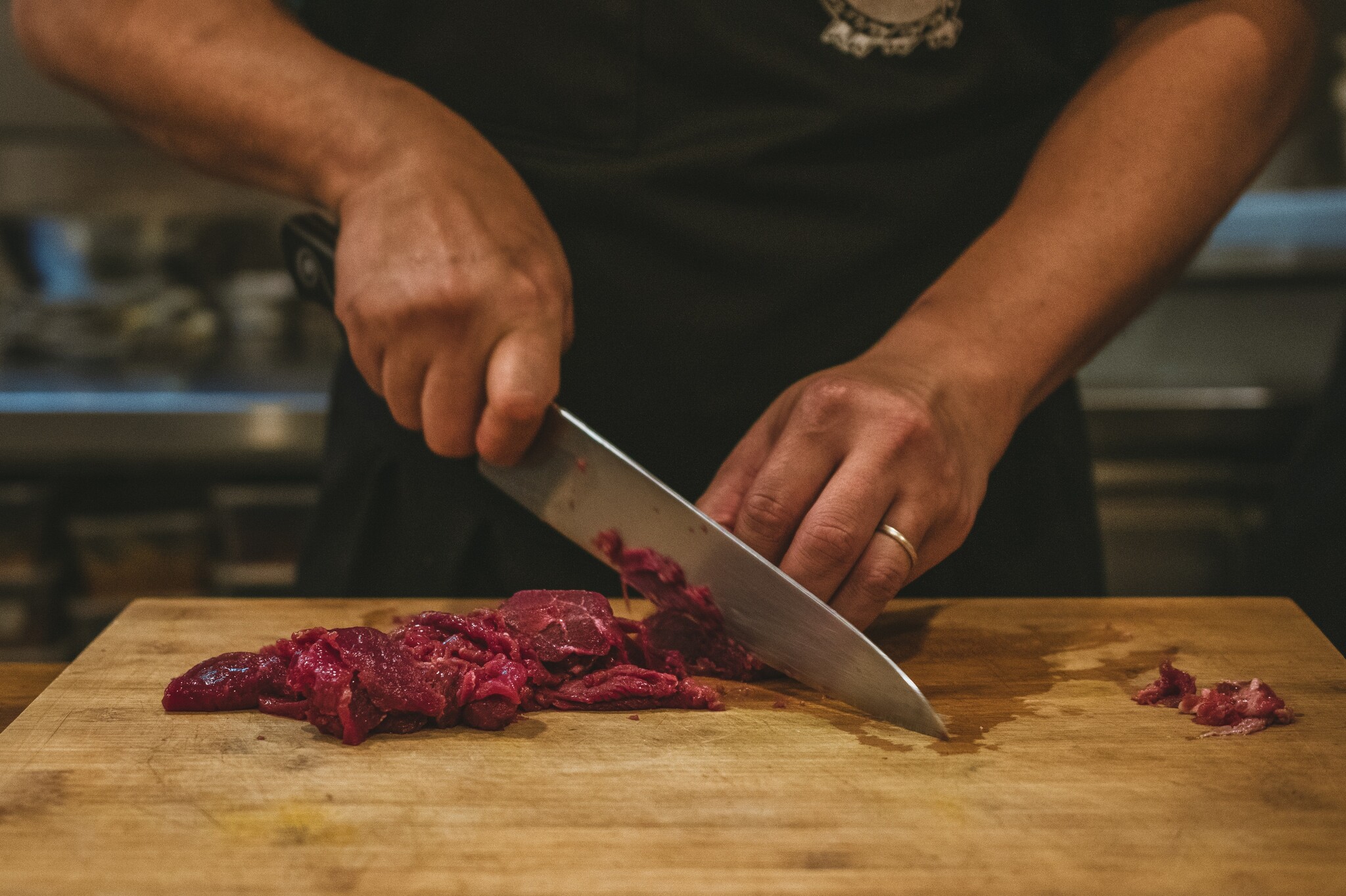 A man uses a chef's knife to cut through red meat on a wooden cutting board.