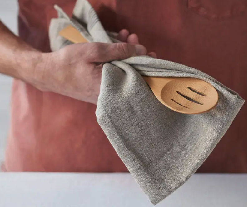 A bamboo slotted spoon is held in a dish towel by a person wearing a red shirt.