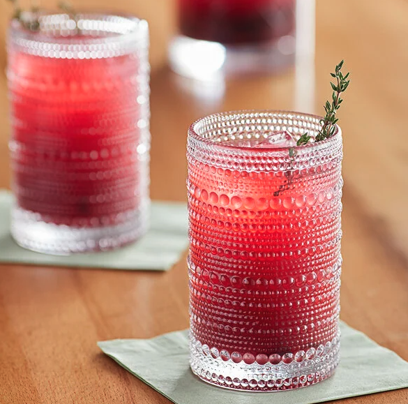 Glass cups sit on a wooden table with a red drink inside. 